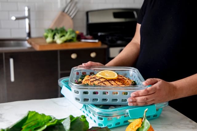 Eine Person bereitet mit Meal Prep gesunde Mahlzeiten im Voraus vor, indem sie frische Zutaten schneidet und in Behälter packt.