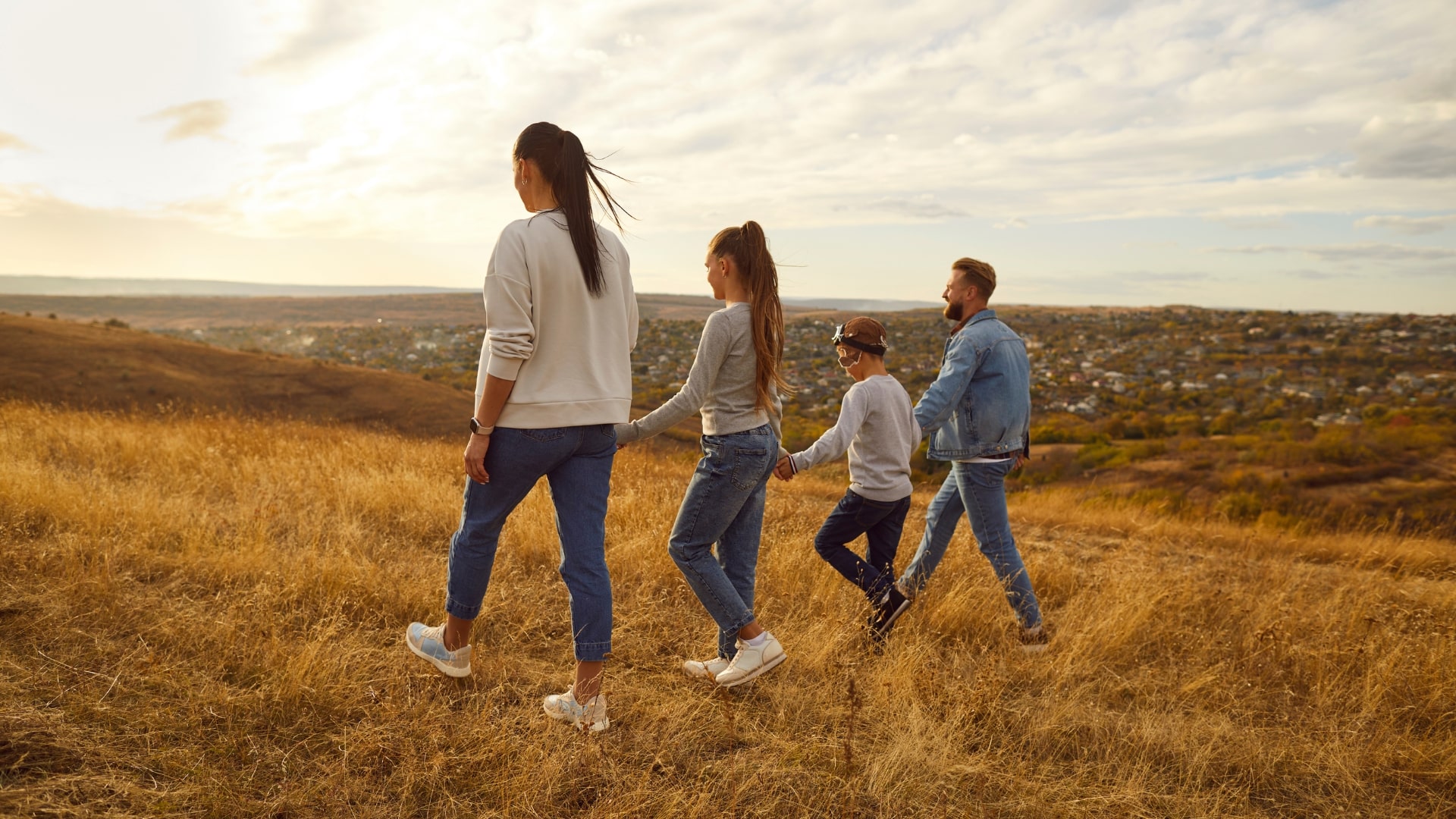 Familie wandert gemeinsam auf einem Hügel mit Blick auf eine Stadtlandschaft – Aktivitäten nach Wundpflege einer Akne Inversa Operation.