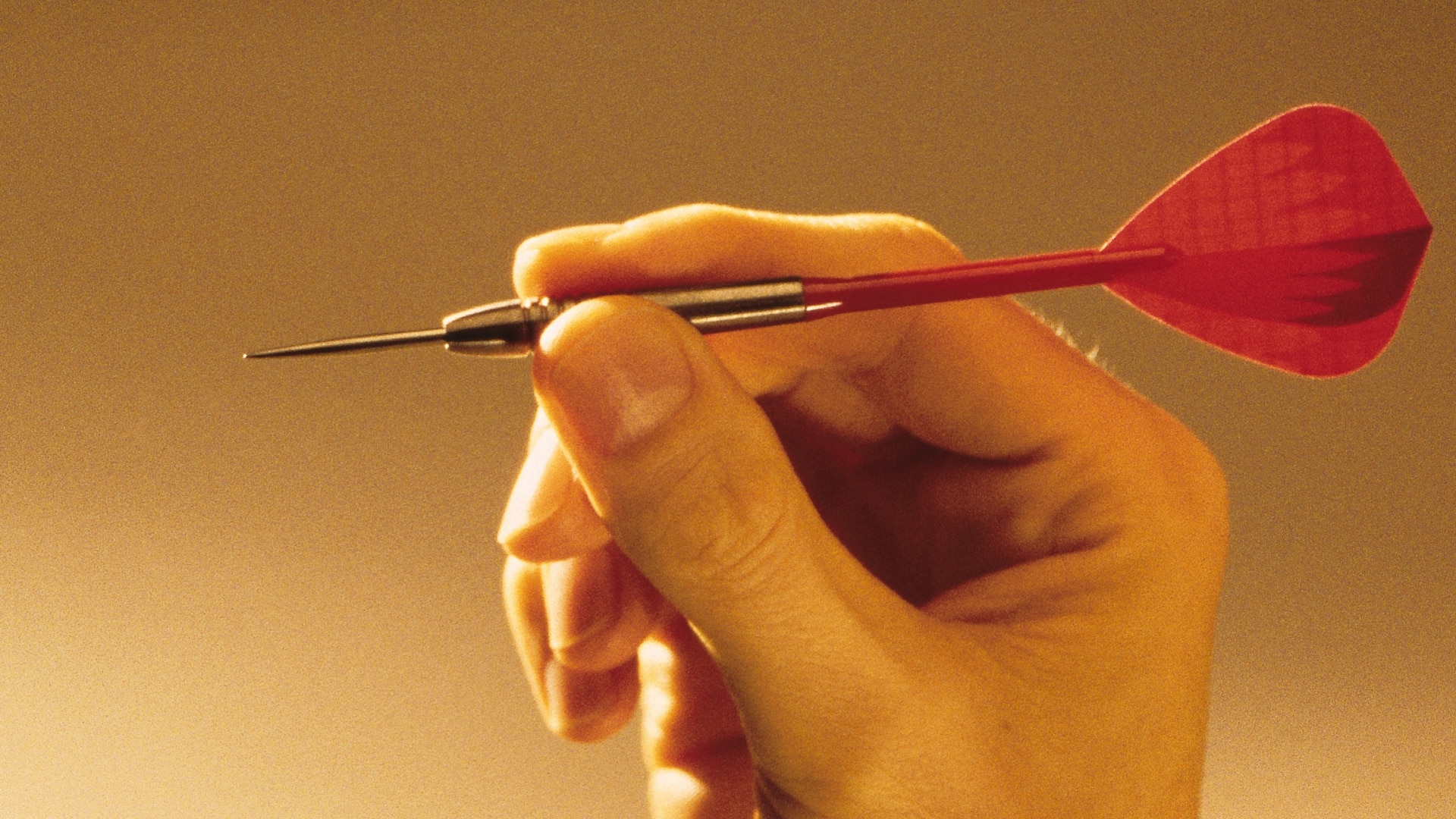 Hand hält einen roten Steel-Dart korrekt griffbereit (Dart Wurftechniken Tipps).