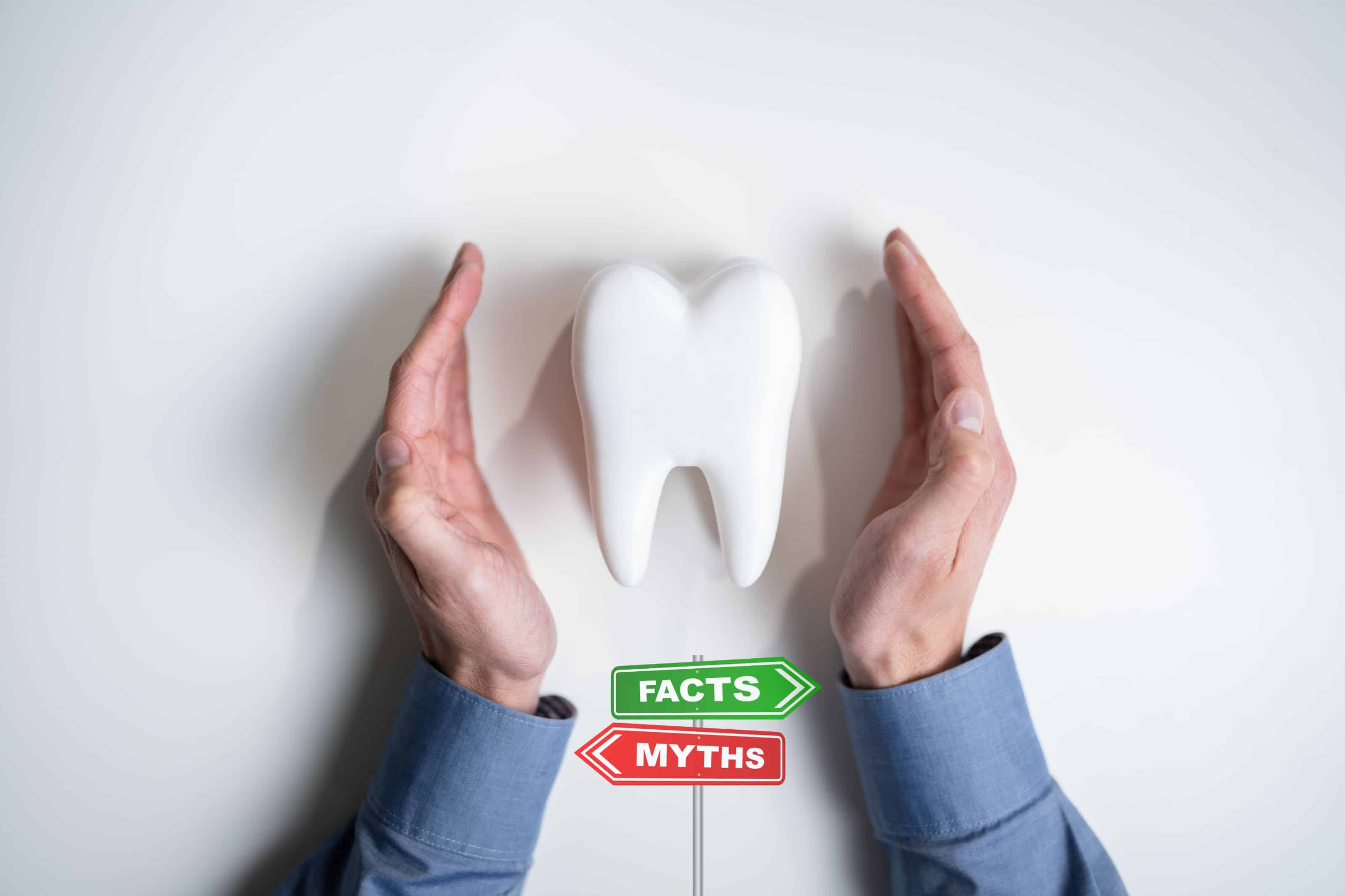 Zahn umgeben von Händen mit Schildern Facts und Myths – Symbol für Mythen und Fakten zur Zahngesundheit und Ölziehen.