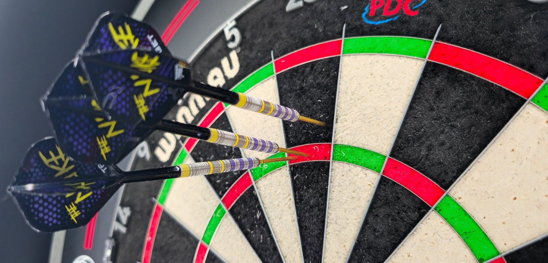 Drei Luke Littler Loadout Darts stecken eng gruppiert im Triple-Ring eines Turnierboards, Flights mit „The Nuke“-Logo gut sichtbar.	