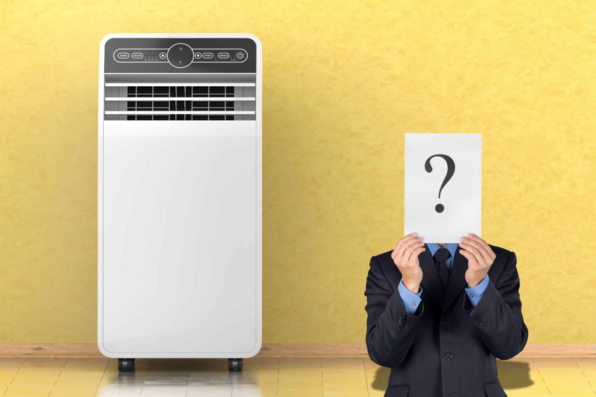 Mann im Anzug hält Schild mit Fragezeichen neben mobiler Klimaanlage – symbolisiert Unsicherheit vor dem Kauf.