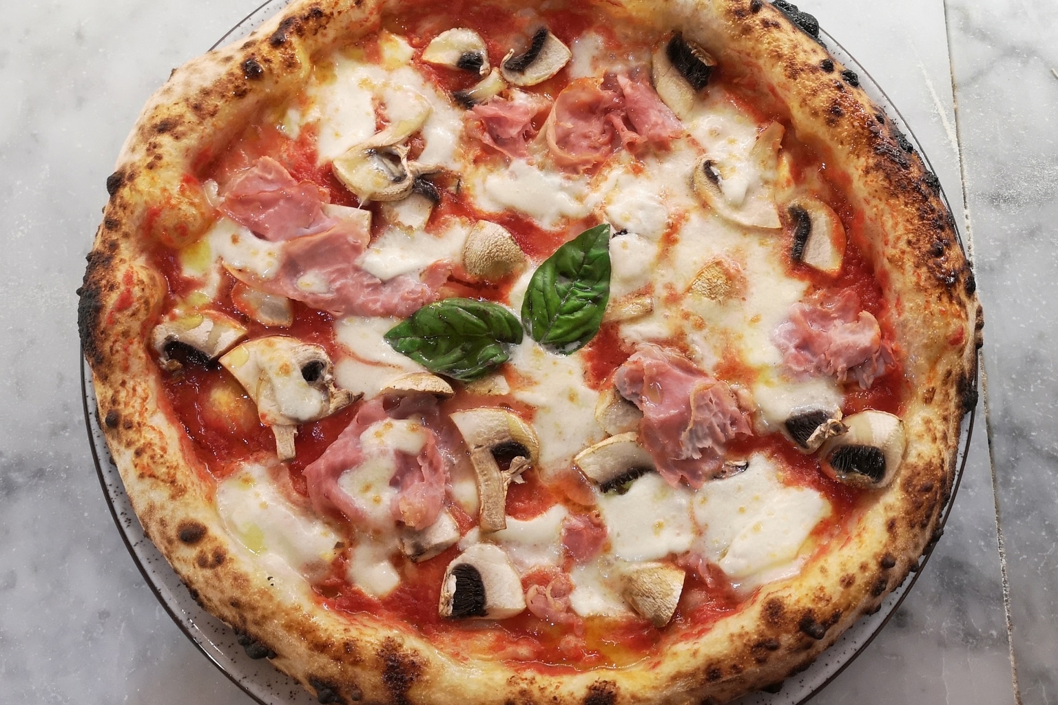 Frisch gebackene 30-cm Pizza mit Tomatensauce, Mozzarella, Prosciutto, Champignons und Basilikum – direkt aus dem Ninja Artisan MO201EU Outdoor-Pizzaofen, goldbraun und knusprig.