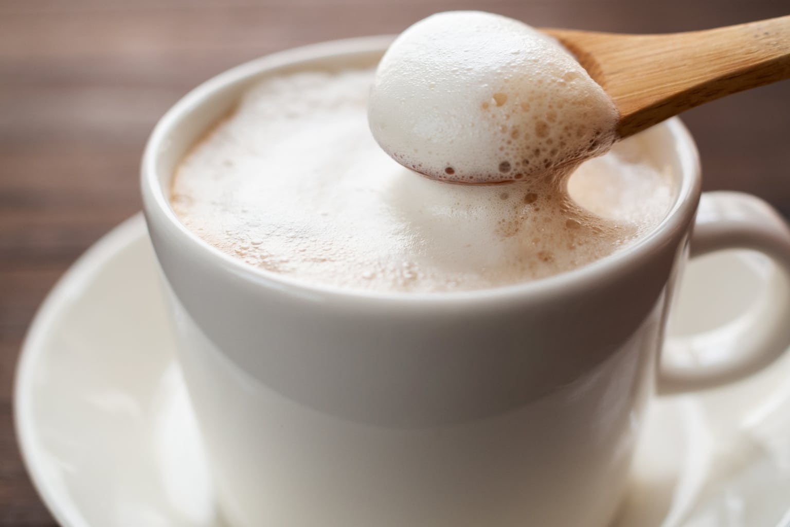 Milchaufschäumer unter 50 Euro Empfehlung – feinporiger, cremiger Milchschaum in weißer Tasse; Holzlöffel hebt Mikroschaum an.