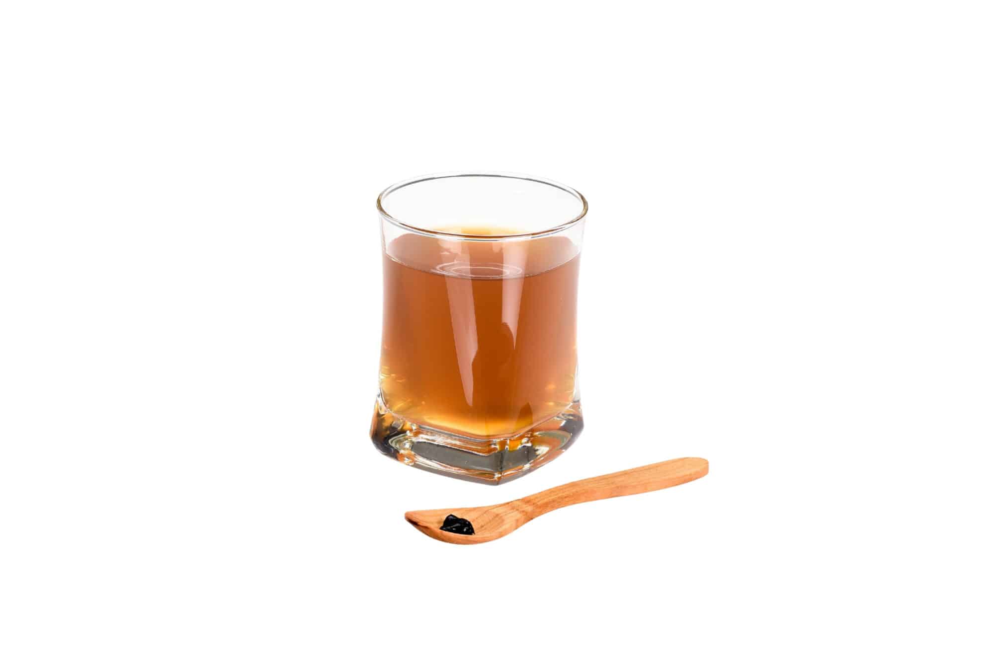 Holzlöffel mit kleinem Klecks Shilajit‑Harz vor Glas mit gelöster Shilajit‑Mischung