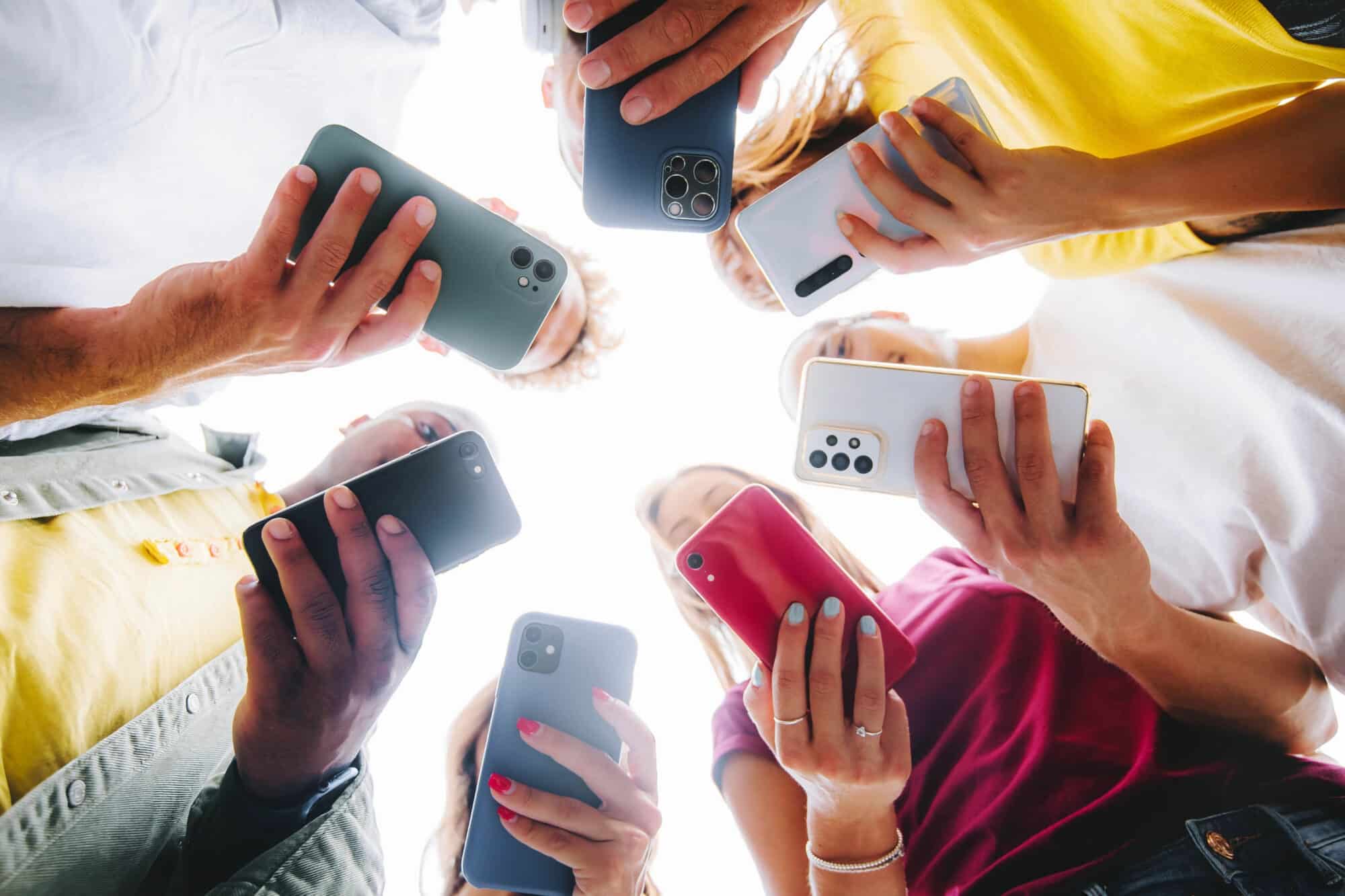 Gruppe von jungen Erwachsenen bildet einen Kreis und schaut gebannt auf ihre Smartphones – Sinnbild für Alltags-Smartphoning und den Bedarf an Digital Detox