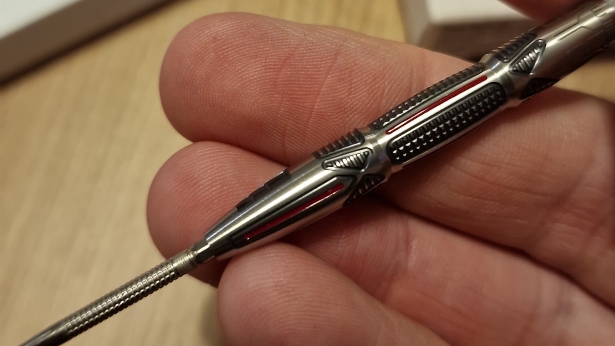 Nahaufnahme des Target Star Wars X-Wing Steeldarts-Barrels mit schwarzem und rotem Grip, gehalten zwischen Daumen und Fingern.