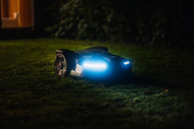 Leiser Mähroboter im kleinen Garten bei Nacht mit eingeschalteten Lichtern – Lautstärke und Sicherheit für Igel im Blick.